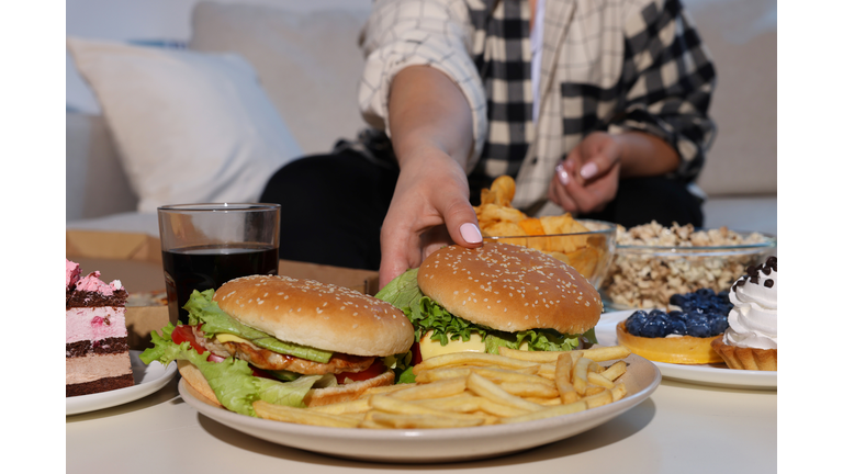 Overweight woman taking burger at home, closeup
