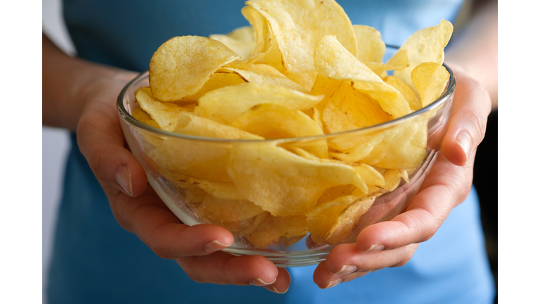 Crispy fried fatty potato chips in a glass bowl or plate, on a white background or table. Chips in the hands of a woman or a teenage girl, she eats them. The concept of an unhealthy diet and lifestyle, the accumulation of excess weight.