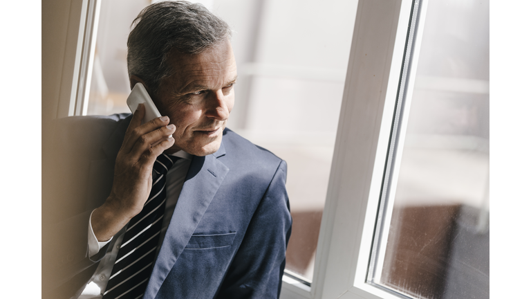 Smiling mature businessman on cell phone looking out of window