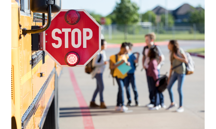 Group of school children talk outside bus