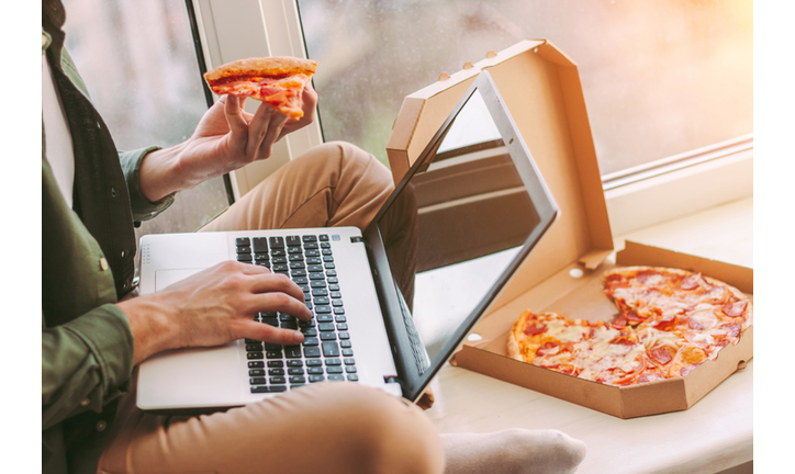 Businessman freelancer surfing internet on laptop and eating pizza