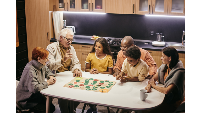 Large happy multiracial family playing board game by table