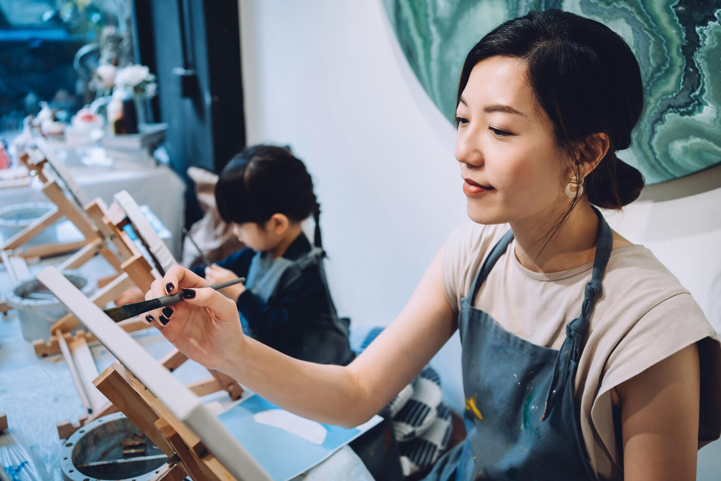 Young Asian mother and little daughter having a painting class together. Painting on a canvas with paintbrush and colourful acrylic paints. Having a relaxing afternoon