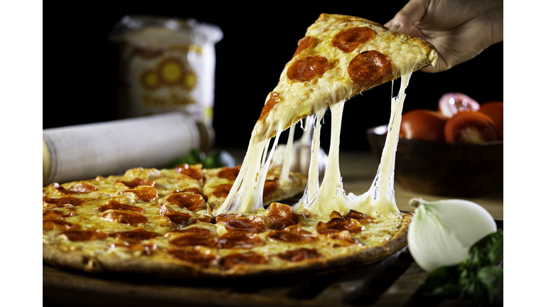 Person getting a piece of cheesy pepperoni pizza