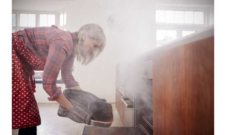 Middle aged woman opening smoke filled oven in the kitchen