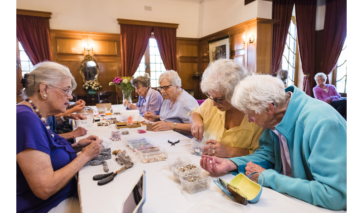 Group of senior women at a table making handmade jewellery with beads