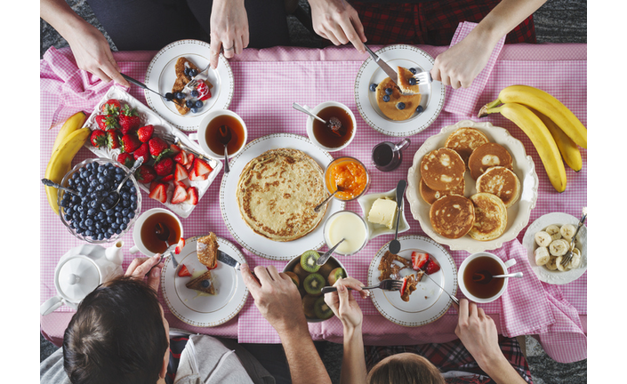 Breakfast table. Flat lay of eating peoples hands over breakfast table with crepes, pancakes, tea and berries.