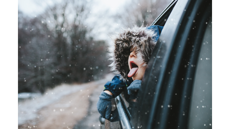 Boy on a road trip. the little boy is looking from the car window in winter , opened his mouth and pulled out his tongue, catches snowflakes