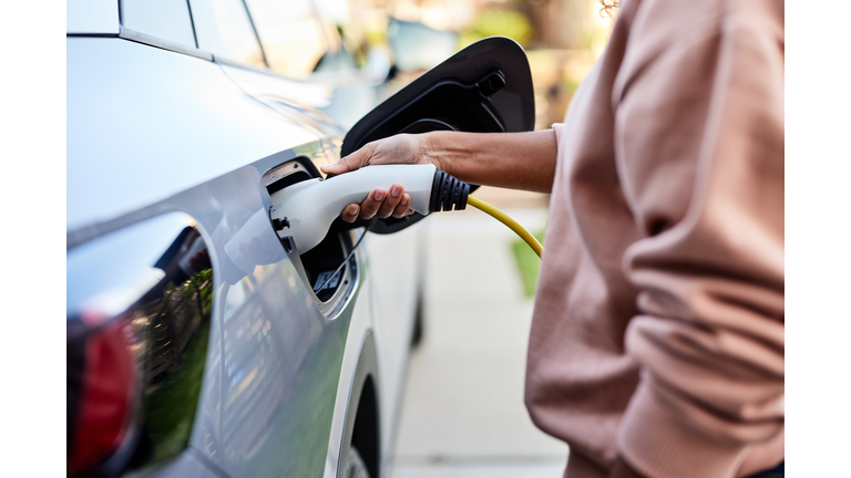 Midsection of woman plugging cable in electric car