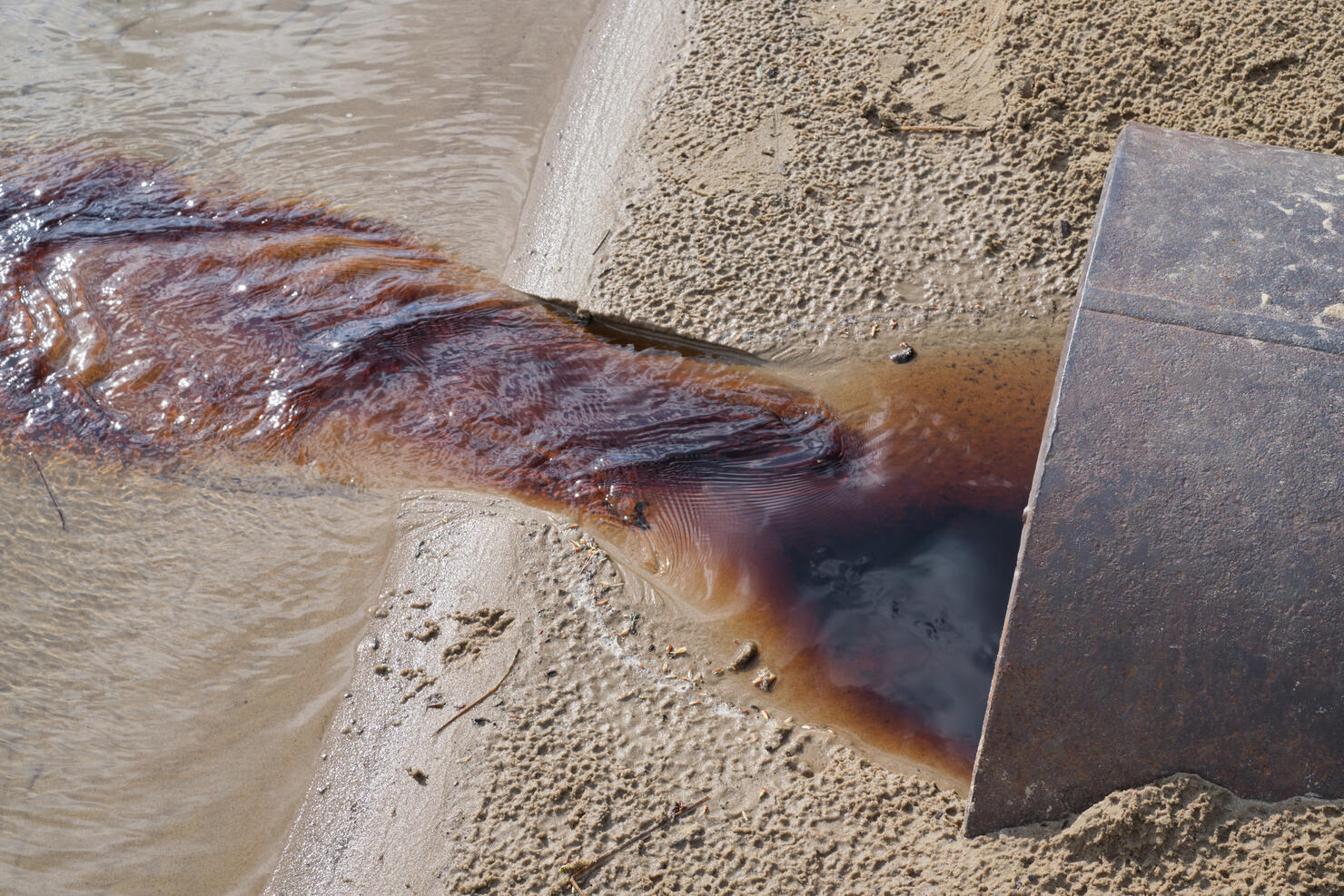 waste water running  from a out of a metal pipe onto pond. Sewage drains into the river. Environmental pollution. Ecological catastrophe and disaster.