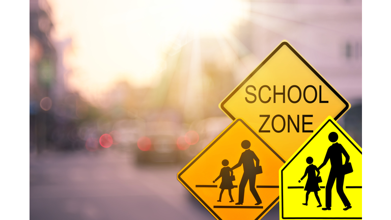 School zone warning sign on blur traffic road with colorful bokeh light abstract background. Copy space of transportation and travel concept. Vintage tone color style.
