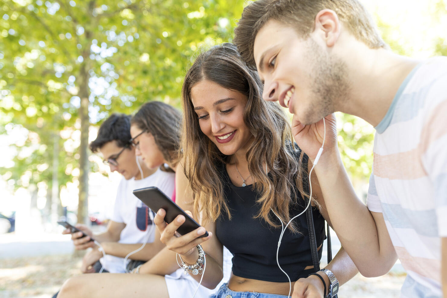Group of friends at a park having fun together and listening to music on cell phones