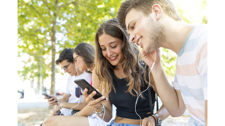 Group of friends at a park having fun together and listening to music on cell phones