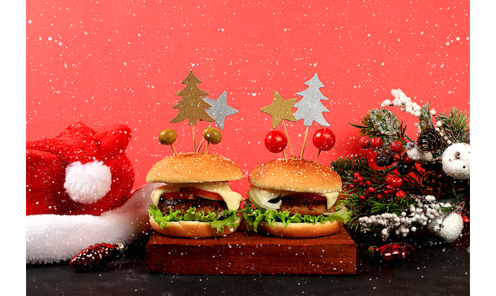 Two Christmas burgers with tomatoes, olives, cream cheese, onions, cutlets on a holiday table with a live Christmas tree and decorations, New Year's food and dishes. cafe advertising,