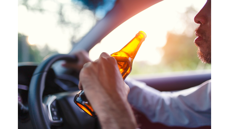 Drunk asian young man drives a car with a bottle of beer