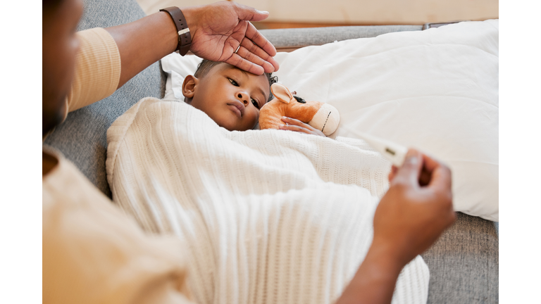 Sick, flu and cold child in bed, sad and ill with allergy and unwell at home with his worried mother. Parents hand on son's forehead for his temperature as she checks his fever with a thermometer