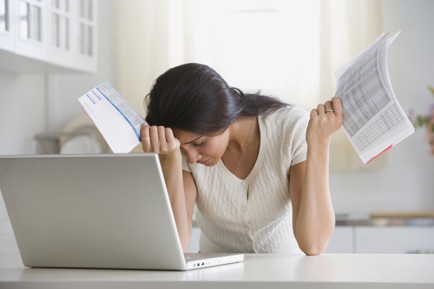 Overwhelmed woman holding bills in front of laptop