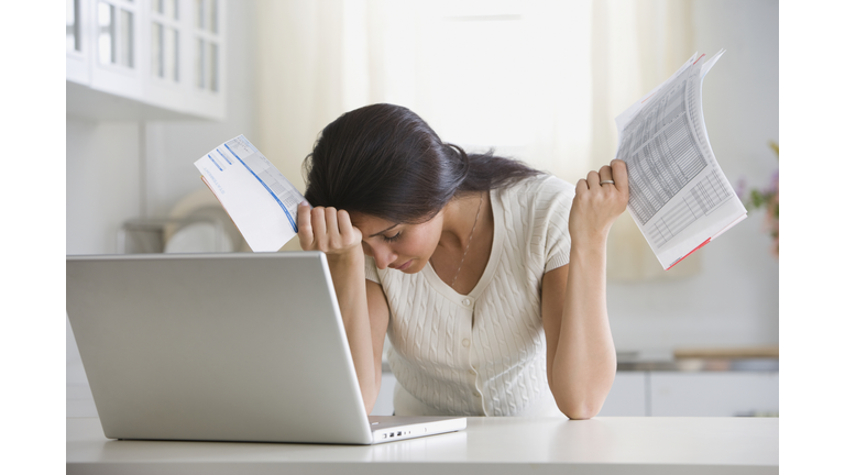 Overwhelmed woman holding bills in front of laptop