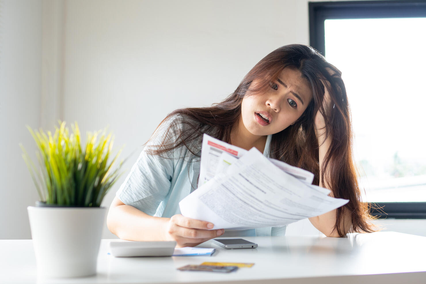 stressed young pretty woman headache holding credit card invoice in hand and worried about bill in home office, plan money cost saving, shopping online