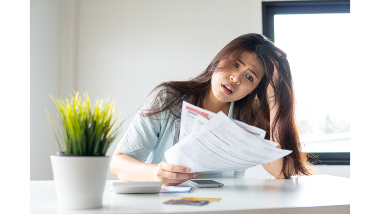 stressed young pretty woman headache holding credit card invoice in hand and worried about bill in home office, plan money cost saving, shopping online