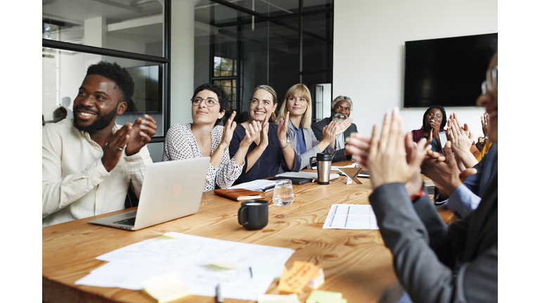 Executives clapping by table in office meeting