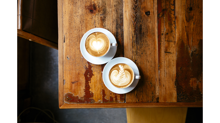 Two cups of coffee with foam latte art on a wooden table seen from above