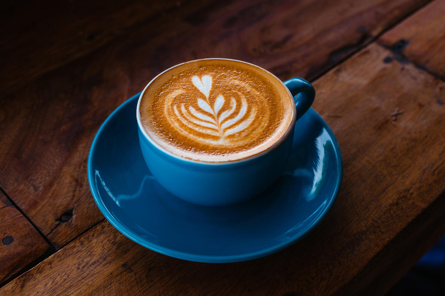 Cappuccino in a blue ceramic mug on a wooden table side view