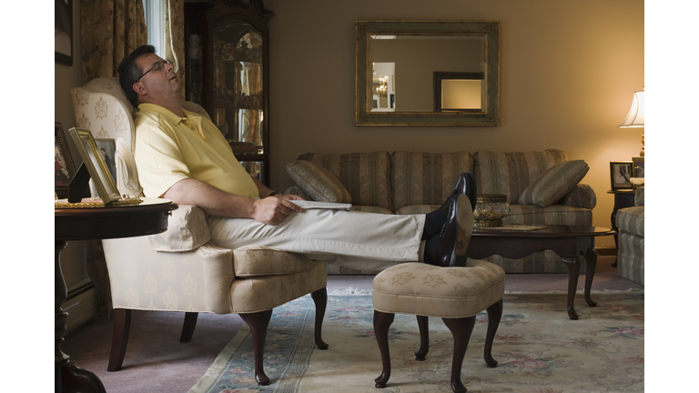 Mature man sleeping in armchair in living room, side view