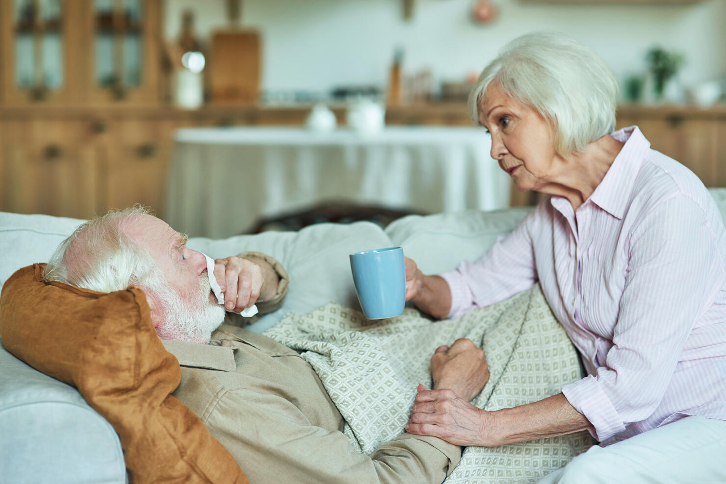 Elderly man is sick and lying on the couch under a warm blanket