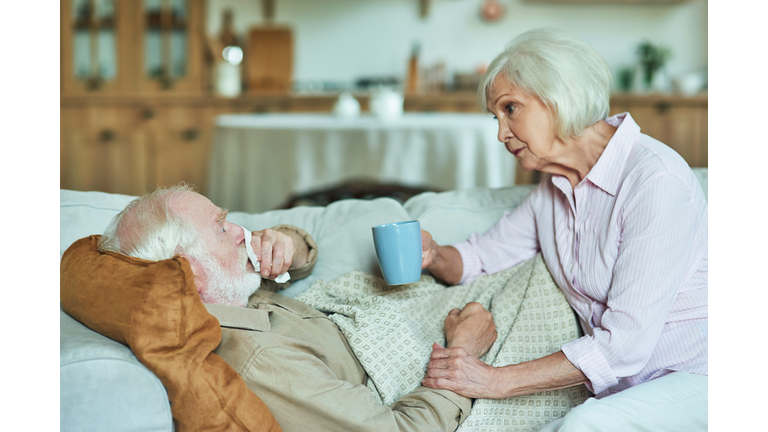 Elderly man is sick and lying on the couch under a warm blanket