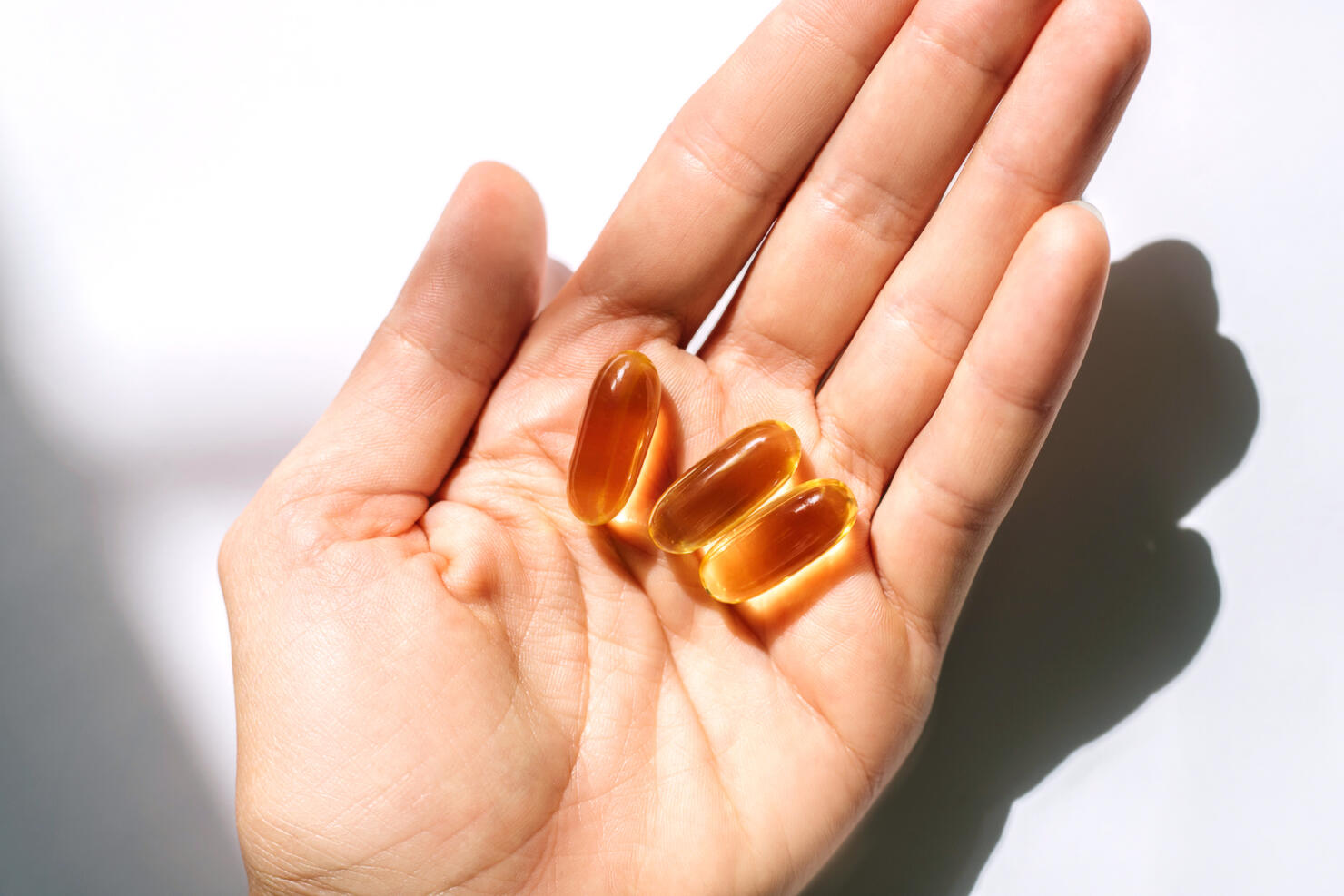Woman's hand holding fish oil supplements on white background.