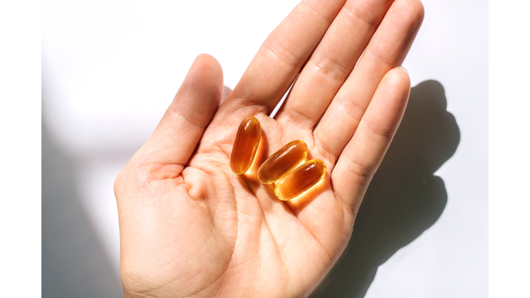 Woman's hand holding fish oil supplements on white background.
