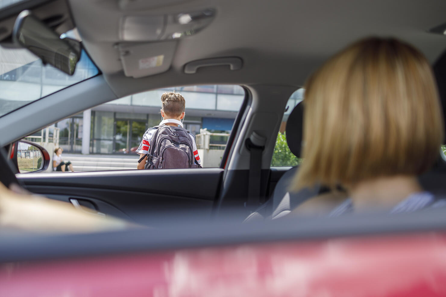 Woman in a car observing her son entering school