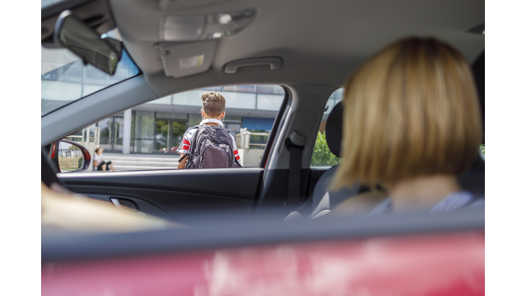 Woman in a car observing her son entering school