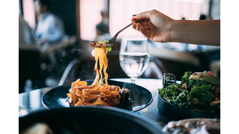 Close up of a woman eating seafood pasta. Sitting in dining table enjoying scrumptious meal in a restaurant. Eating out lifestyle