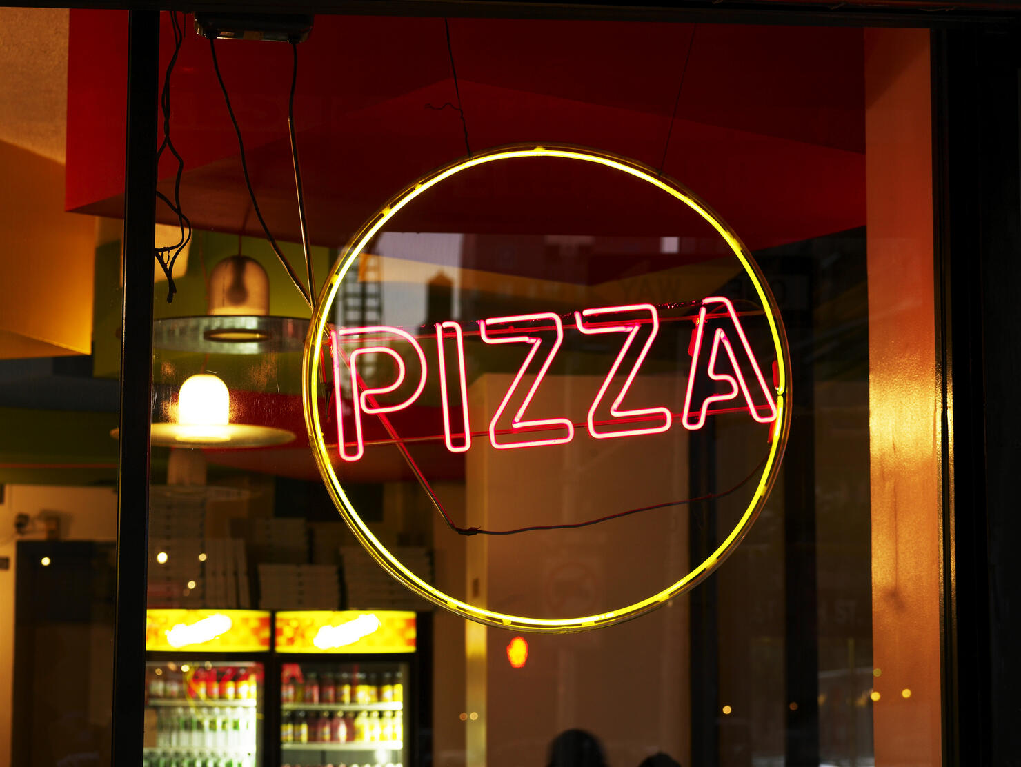 Circular yellow and red pizza sign in window of restaurant