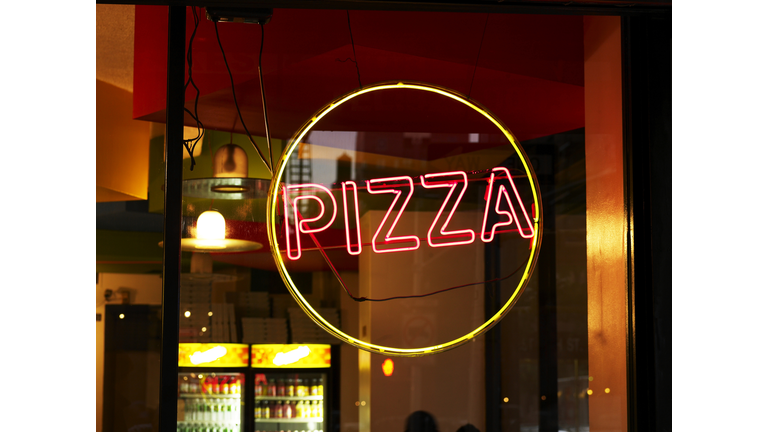 Circular yellow and red pizza sign in window of restaurant