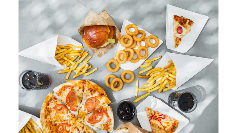 Assorted take out food such as pizza, french fries, onion rings, burger and cola.