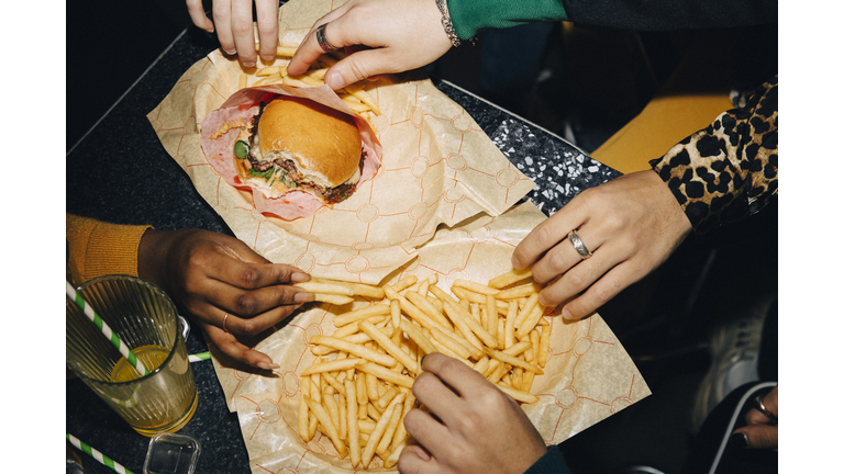 High angle view of friends eating burger and french fries at table in cafe