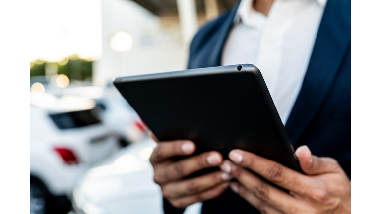 Close-up of car salesman holding a digital tablet at dealership