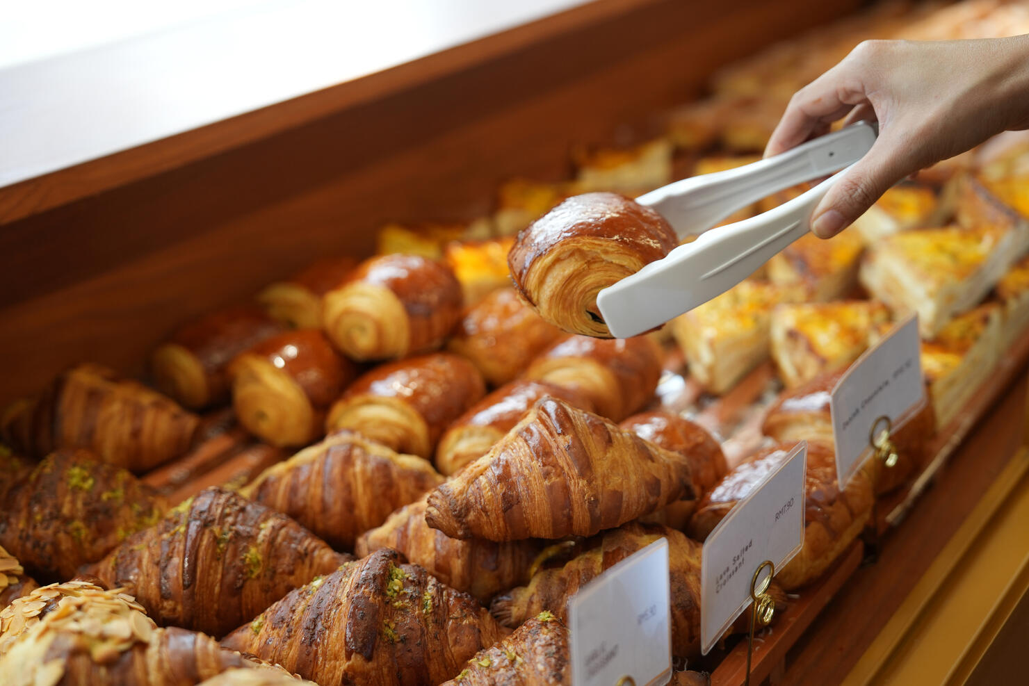 Close-up woman choosing pastry from a bakery store selecting holding a tray and service tong