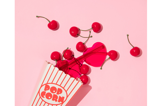 Valentines day creative layout with cherries and heart sunglsses in pop corn box on pastel pink background. 80s or 90s retro fashion aesthetic love concept. Minimal romantic cosmetic idea.