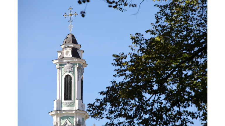 Church spire tower with cross against blue sky with tree in foreground