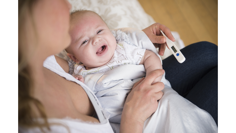 Caucasian mother taking crying baby's temperature