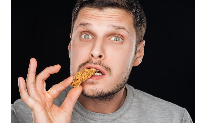 handsome man eating chicken nugget while looking at camera isolated on black