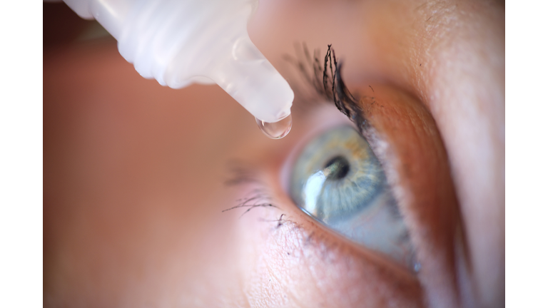 Drops from vial dripping into woman eye closeup
