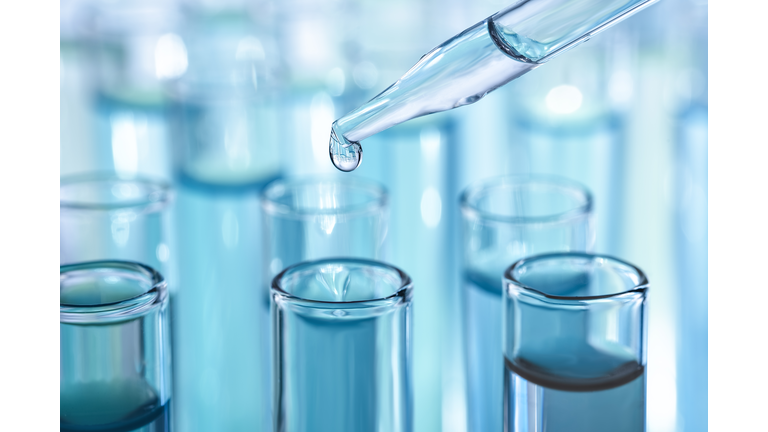 Laboratory glassware with dropper dripping liquid into test tube with light blue liquid close up macro photography.