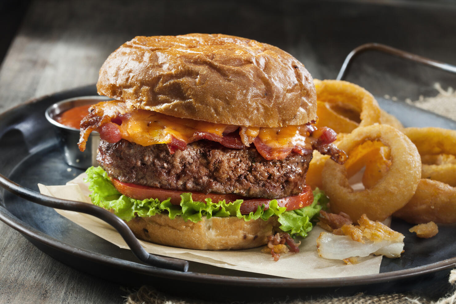 Bacon and Cheddar Burger with Lettuce, Tomato and Thick Cut Onion Rings on a Toasted Onion Bun