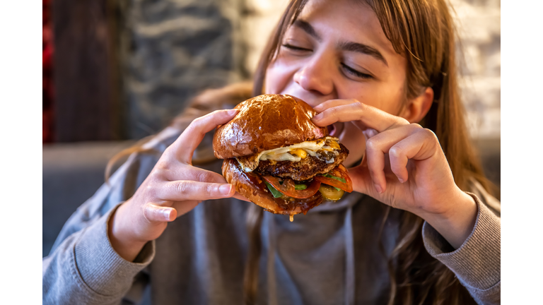 Big appetizing burger with meat in female hands in a cafe.
