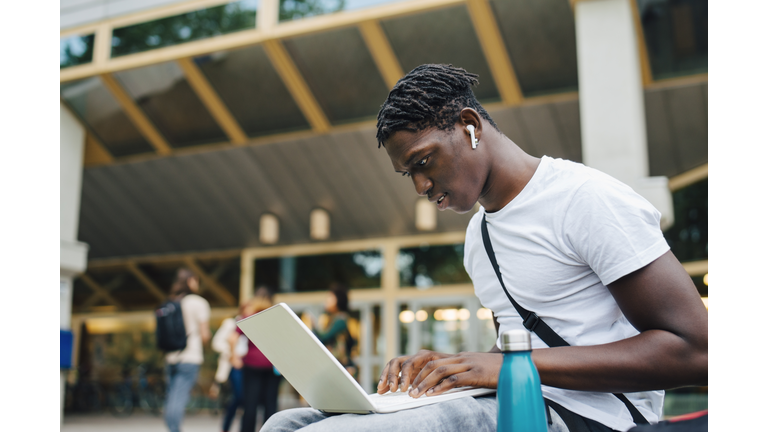 Male college student studying online on laptop in university campus